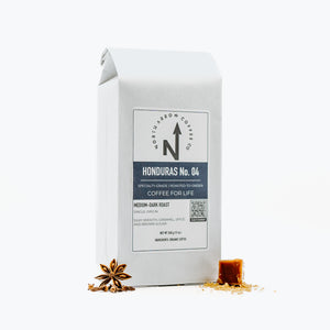 A packaged bag of Honduras No. 04 coffee from North Arrow Coffee Company, with a white label and graphic design, accompanied by visual elements of coffee beans and anise stars.